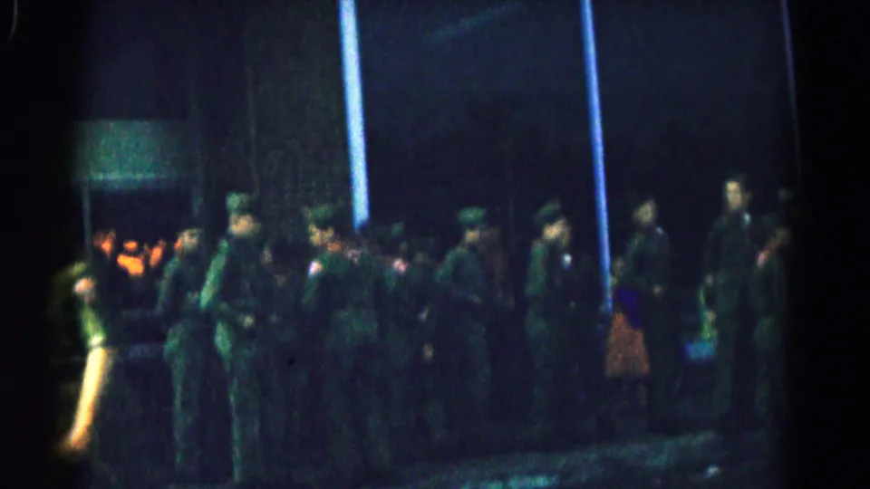 1961 Hagerstown frame of soldiers in green uniforms gathered outside, with a lit building entrance behind them.