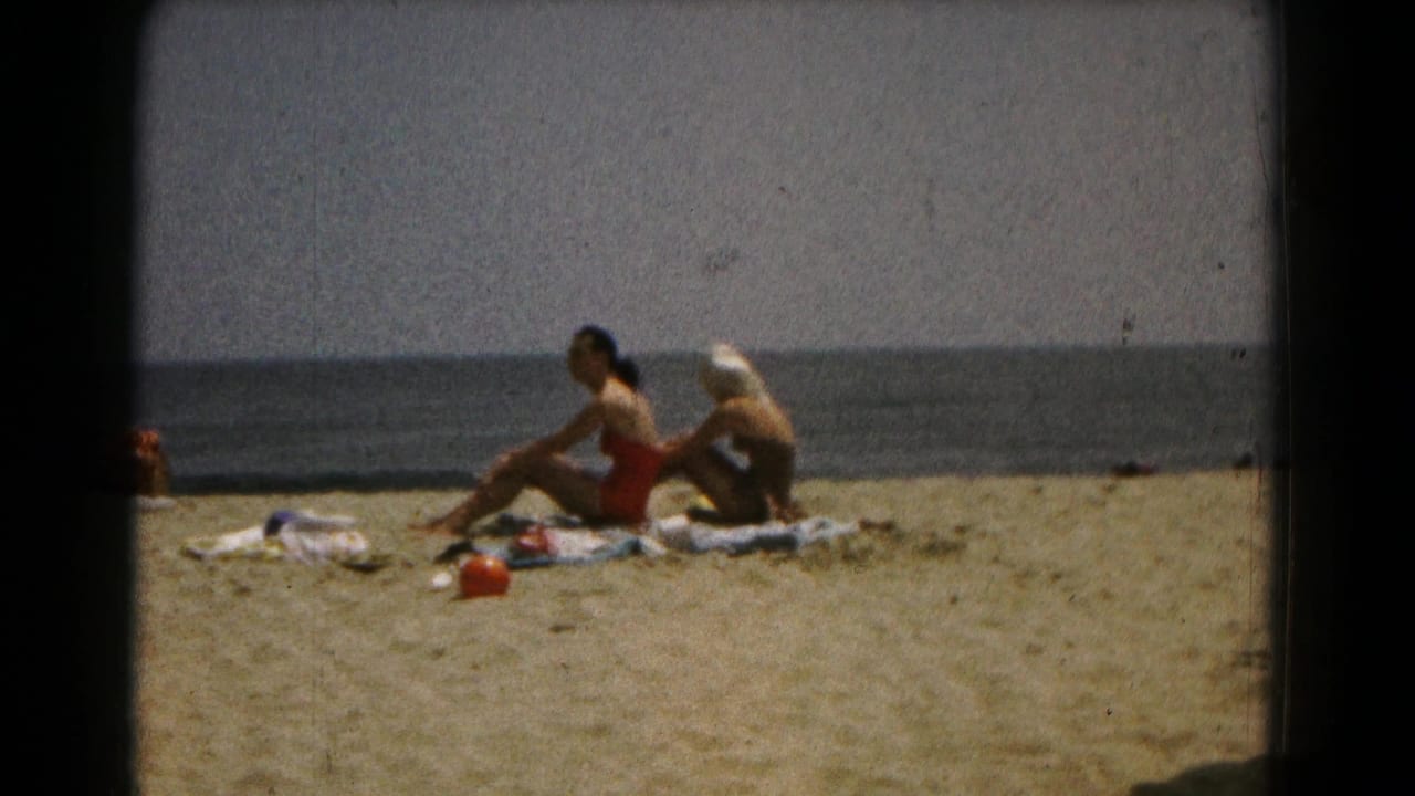 Two women sit on towels on a sandy beach near the ocean horizon.
