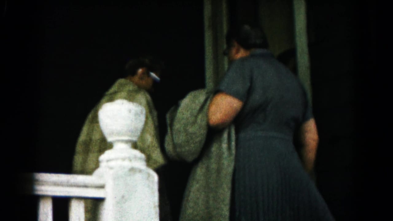 Two women in coats approach a doorway beside a white porch rail.