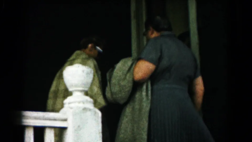 In 1961 Hagerstown home-movie footage, two women in coats move toward a house entrance beside a white porch railing.