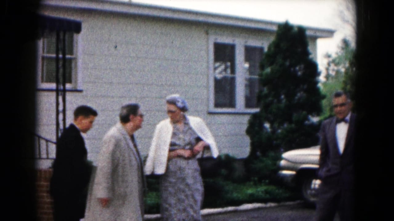 Adults in formal clothing stand outside a light-colored house in Hagerstown, Maryland, with a parked mid-century car nearby.