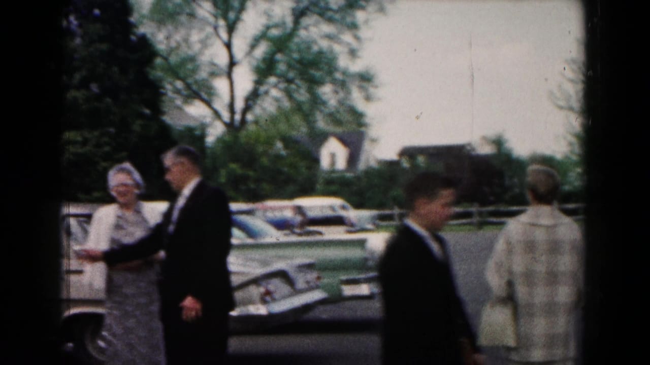 Wedding guests in formal attire standing beside parked cars in an outdoor lot.