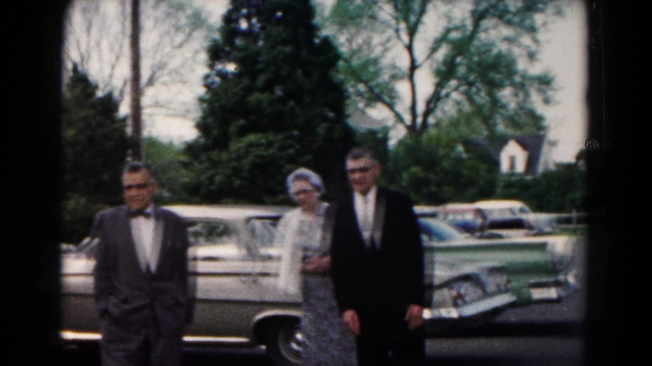 Two men in suits and a woman in a dress appear near a parked car in the 1961 Hagerstown wedding gathering footage.