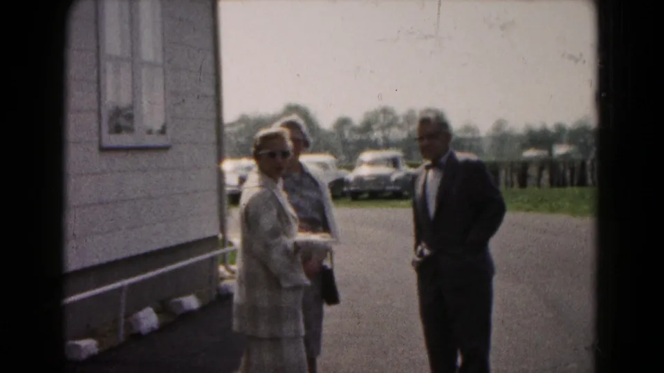 Adults gather near a light-colored building in Hagerstown, Maryland, with early-1960s cars visible across the parking lot.