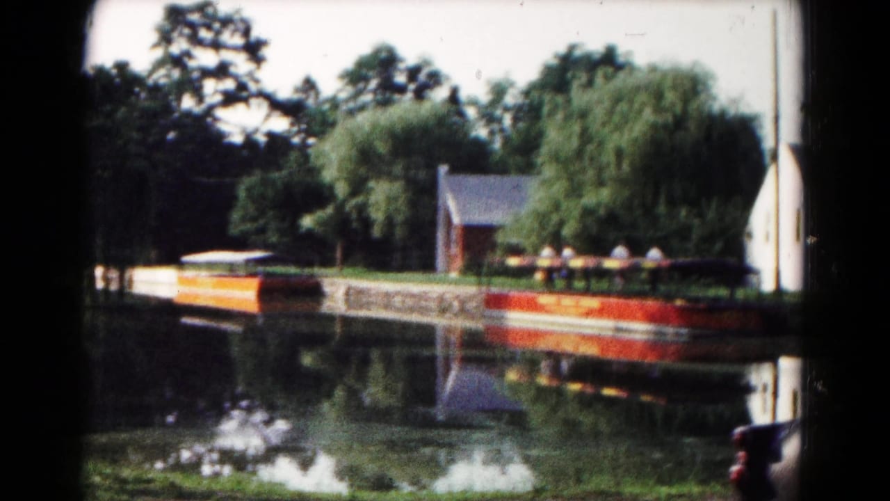 1961 Hagerstown home-movie frame showing a red dock along still water, trees, and a small lakeside building.