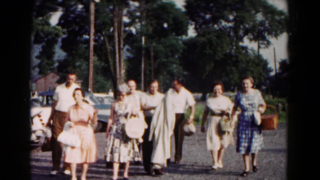 A group of adults walks toward the camera along a roadside in Hagerstown, Maryland, with parked cars and trees behind them.