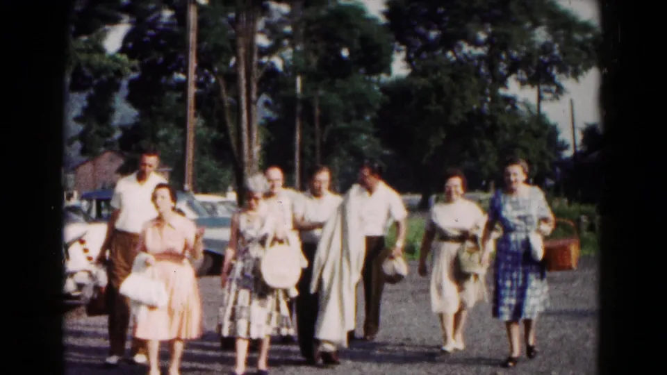A group of adults walks toward the camera along a roadside in Hagerstown, Maryland, with parked cars and trees behind them.