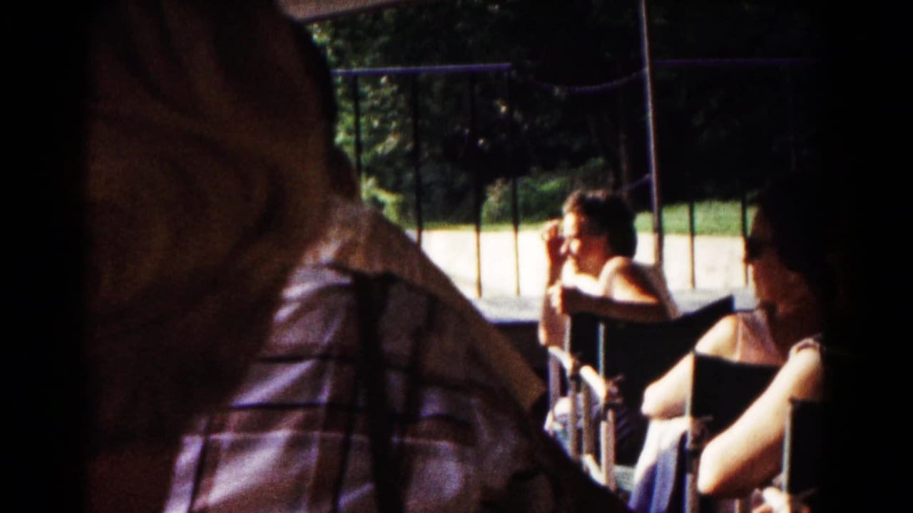 1961 Hagerstown backyard gathering with adults seated in folding chairs under a canopy, partly blocked by a close foreground figure.