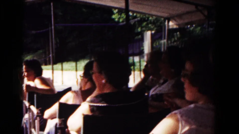 Wider 1961 Hagerstown backyard view showing several adults seated together in folding chairs beneath a canopy beside a bright lawn.