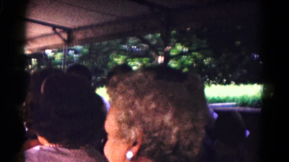1961 Hagerstown home-movie view from inside a covered tram, looking past passengers toward sunlit grass and trees.