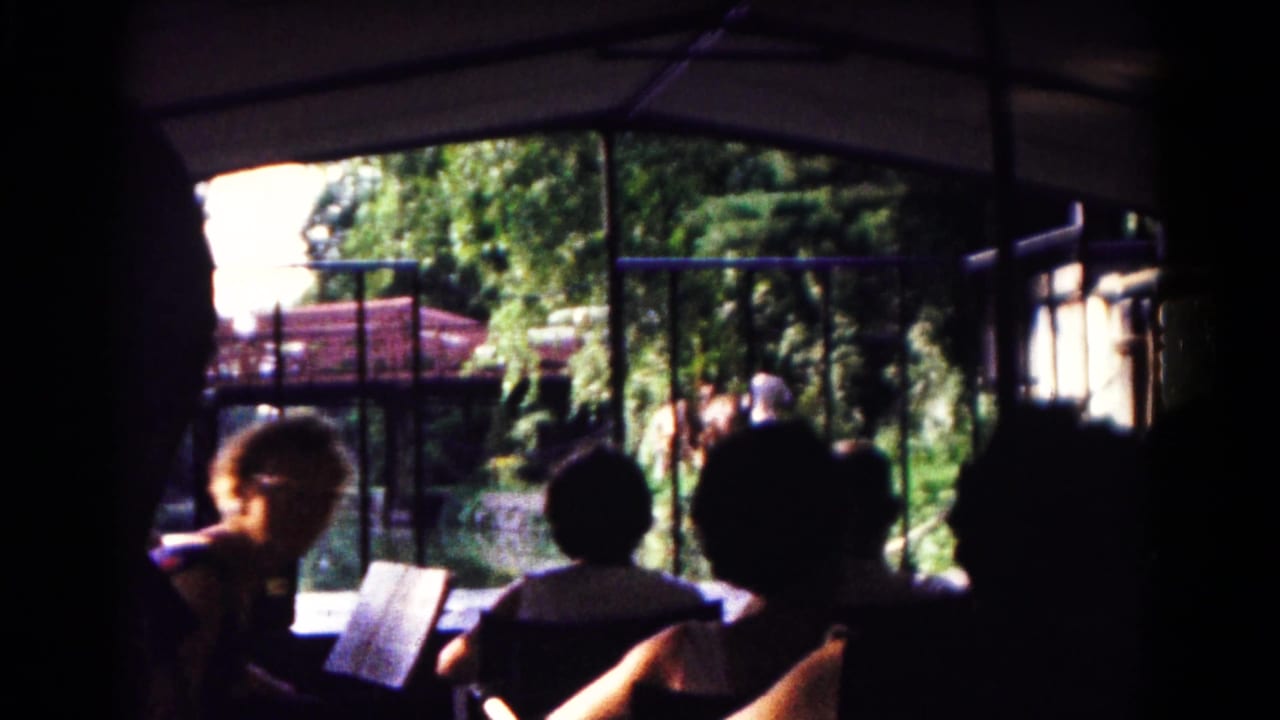 1961 Hagerstown zoo tram view with silhouetted passengers, a guide booklet, railings, trees, and a red-roofed structure beyond the open side.