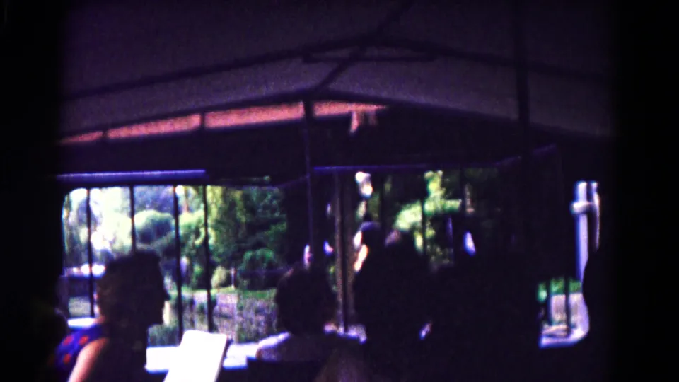 1961 Hagerstown zoo tram scene with dark passenger silhouettes, open windows, metal railings, foliage, and a light guide booklet in the lower foreground.