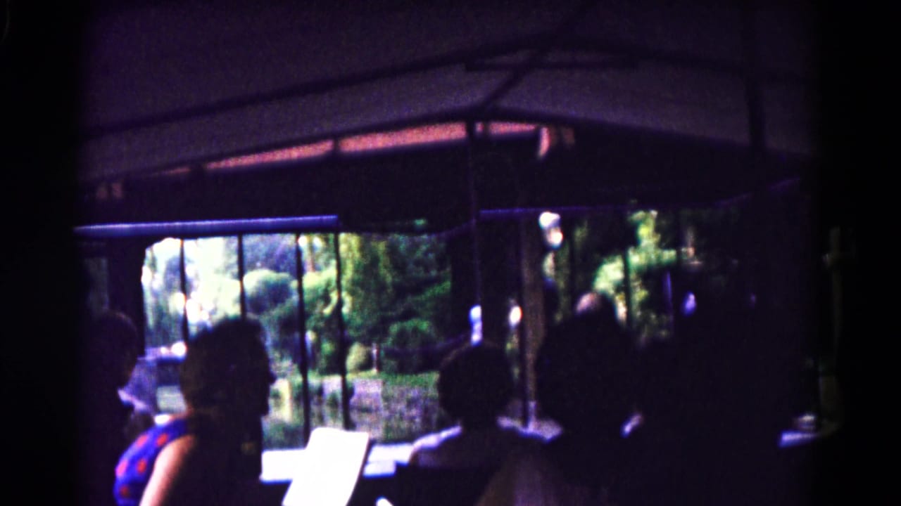 1961 Hagerstown home-movie frame showing riders in silhouette inside a dim attraction with foliage visible beyond the windows.