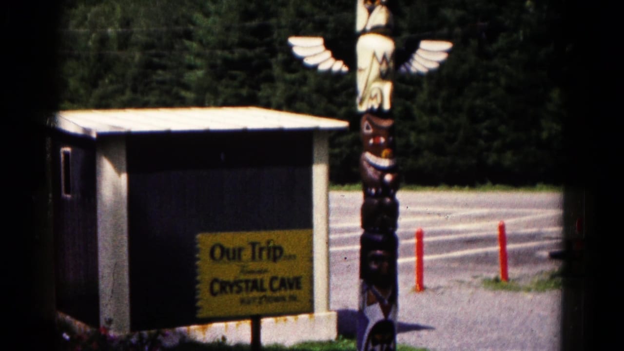 Clearer 8mm view of the Crystal Cave entrance area, with the yellow trip sign, small building, winged totem-style figure, drive, and trees.