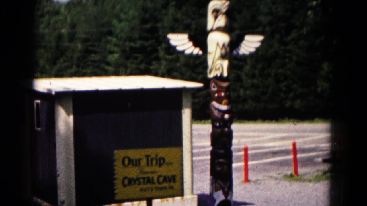Carved eagle totem pole beside a small building with a yellow Crystal Cave trip sign.