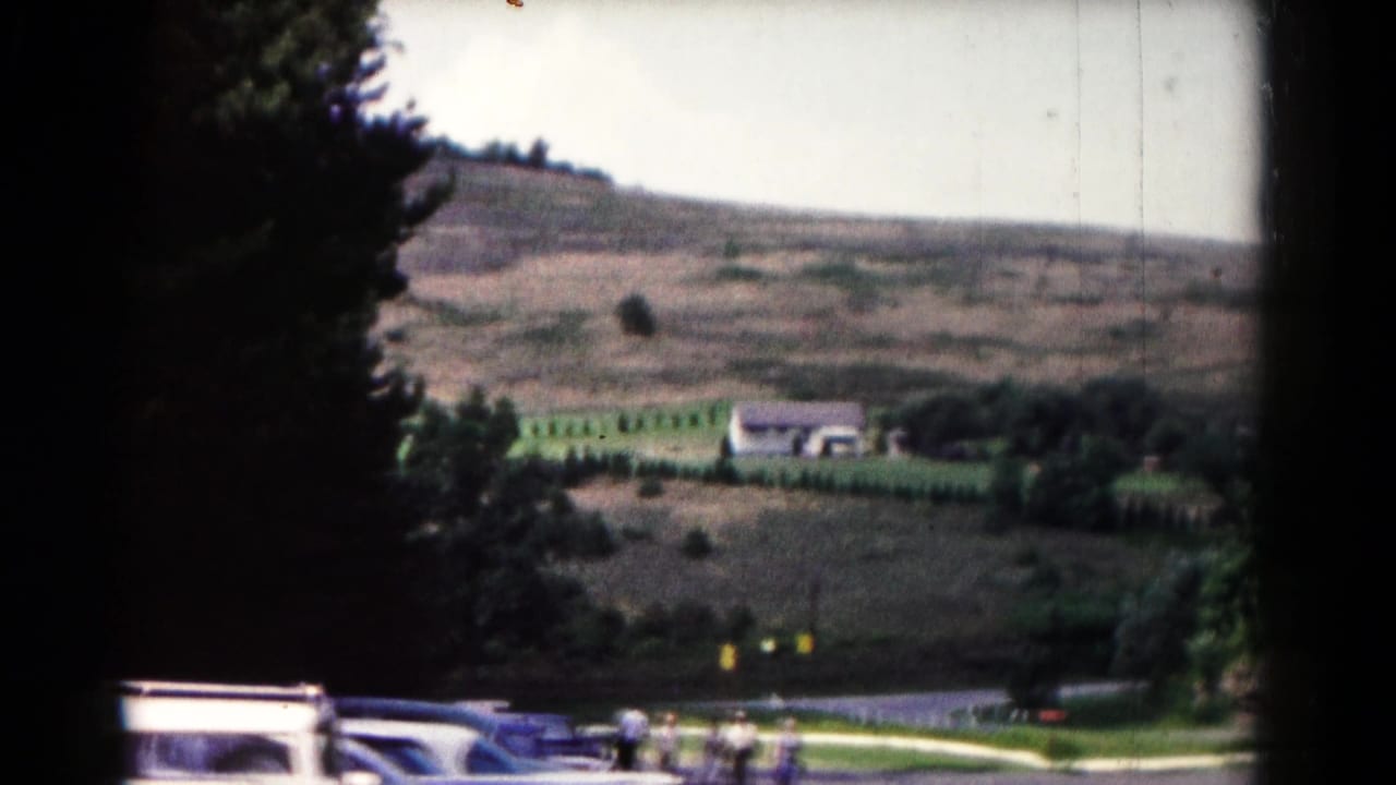 1961 Hagerstown travel frame looking across rolling hills toward a distant house, parked cars, and small figures walking near the road.