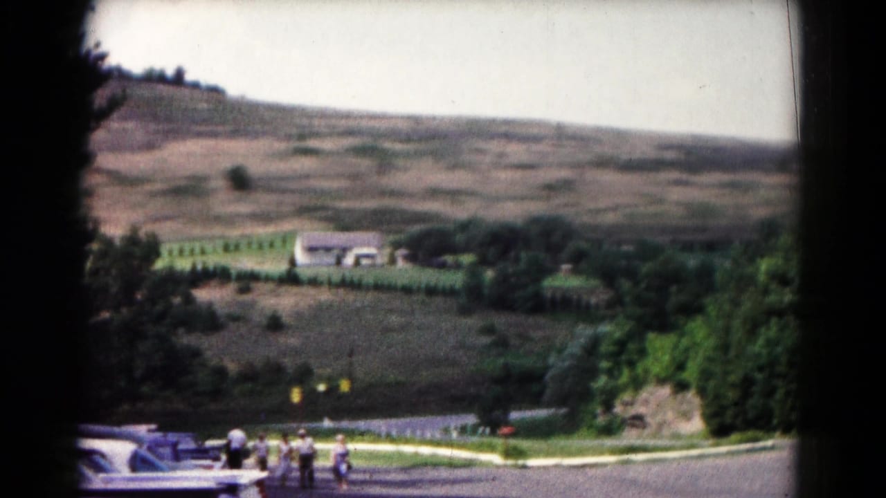 1961 Hagerstown frame showing a rural hillside landscape, parked cars, trees, and a small group of visitors near the road.