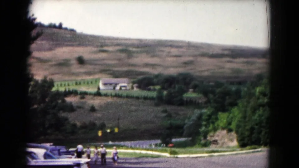 1961 Hagerstown frame showing a rural hillside landscape, parked cars, trees, and a small group of visitors near the road.
