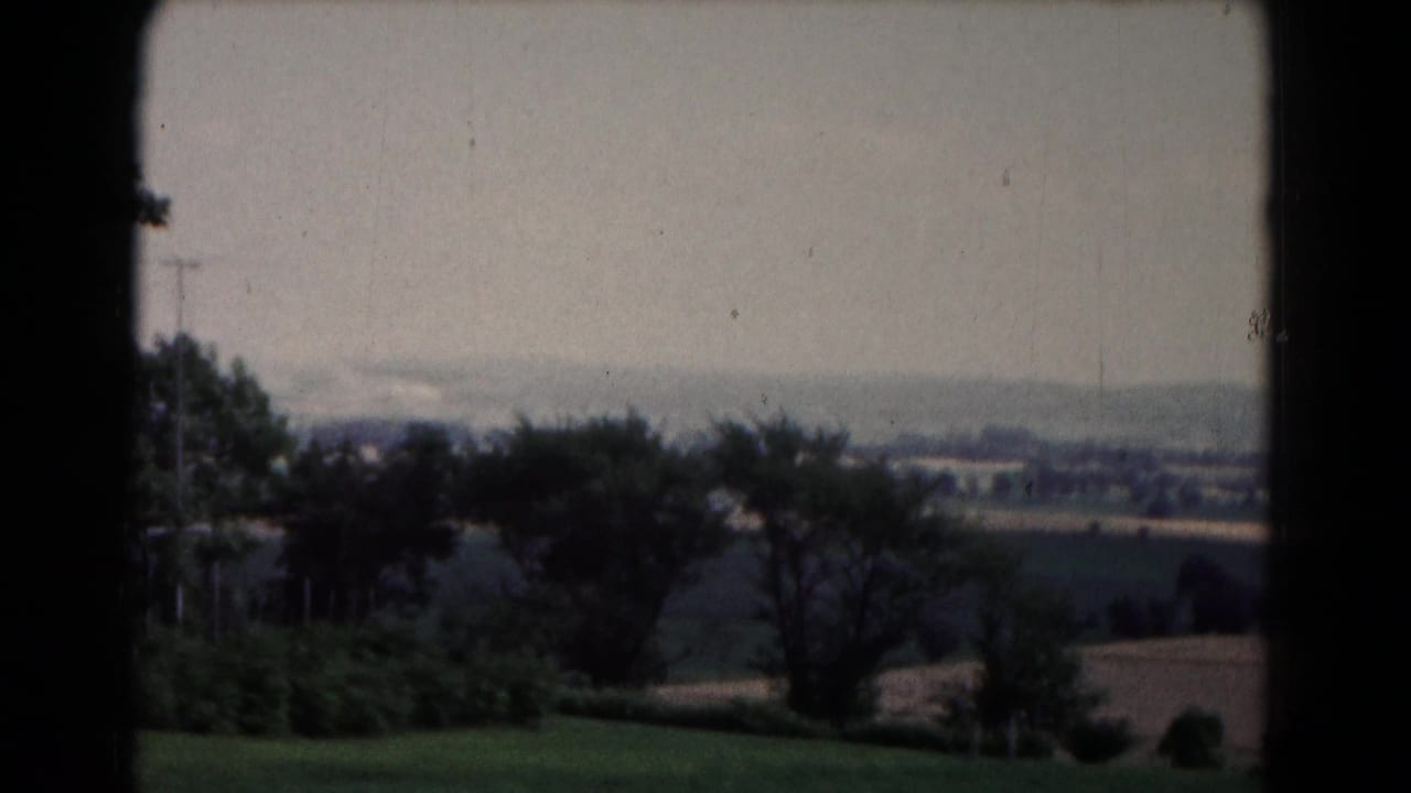 Distant countryside and small-town edge seen beyond trees and open fields.