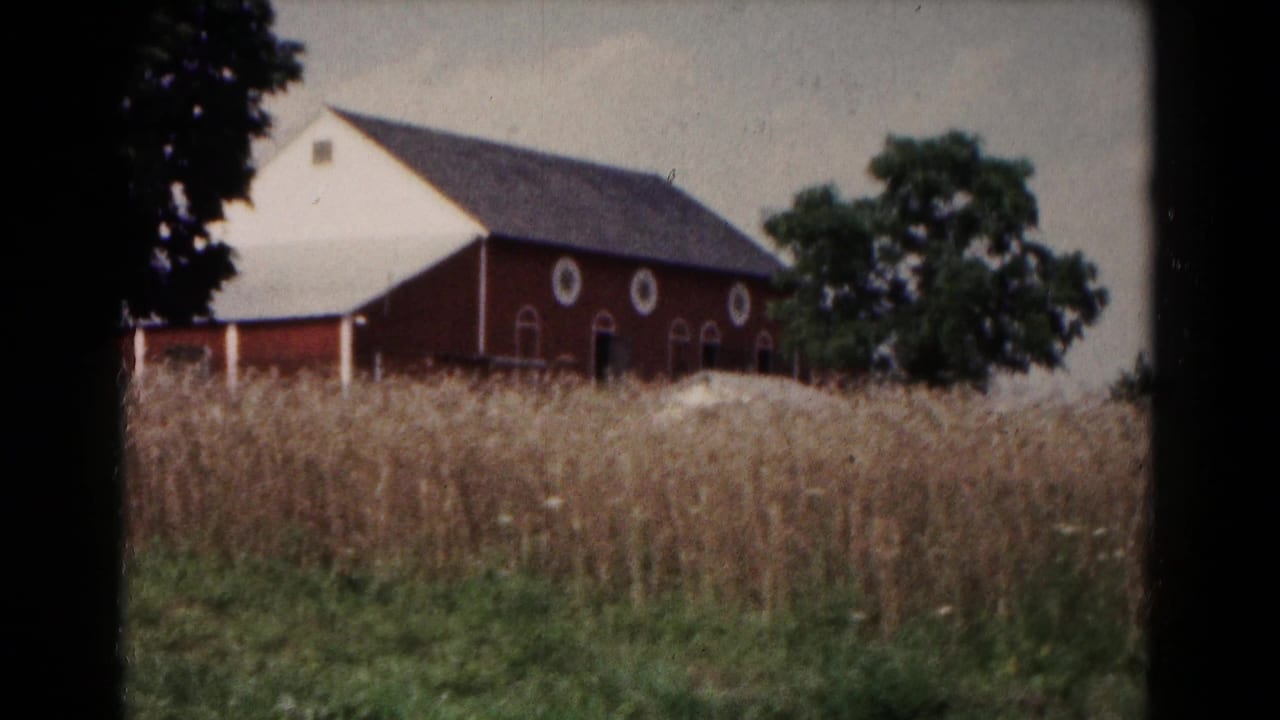 A red barn with white trim stands beyond tall grasses in rural Hagerstown, Maryland, 1961 home-movie footage.