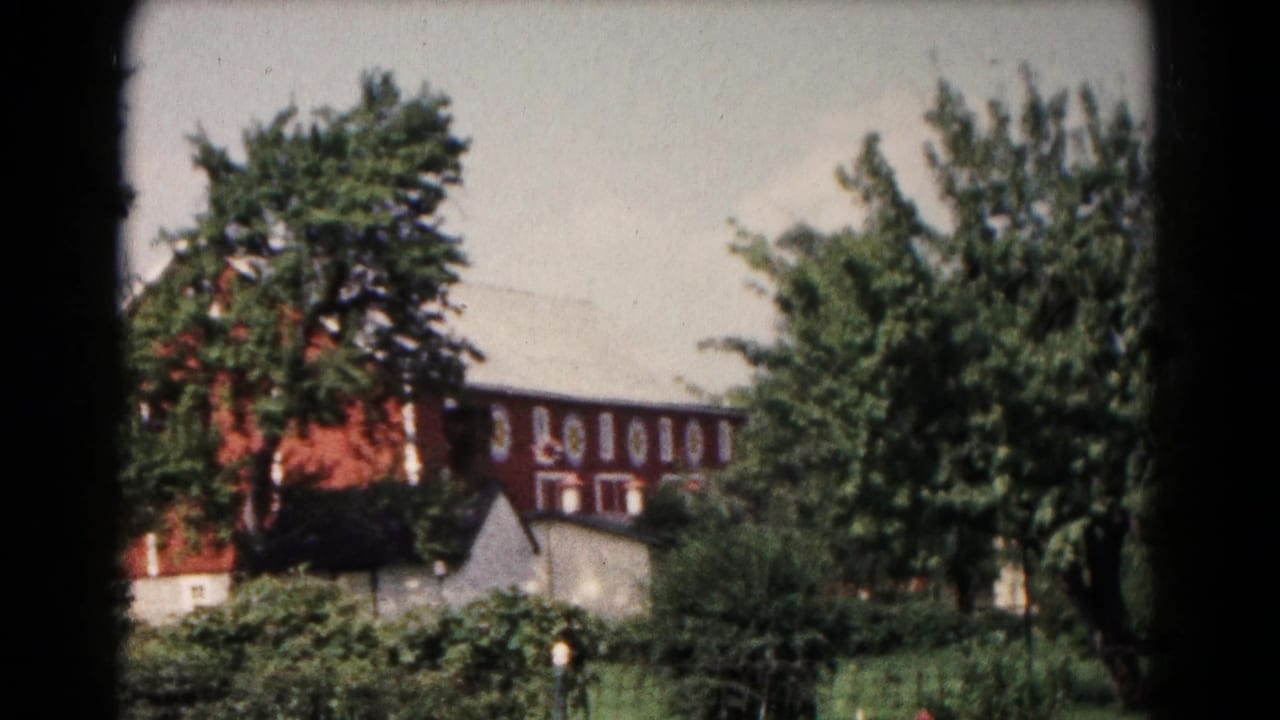 Hagerstown-area 1961 8mm frame showing the red barn partly obscured by trees, shrubs, grass, and a small outbuilding.