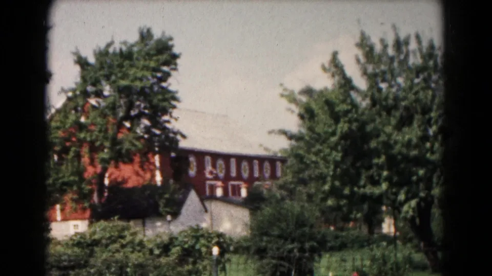 Hagerstown-area 1961 8mm frame showing the red barn partly obscured by trees, shrubs, grass, and a small outbuilding.