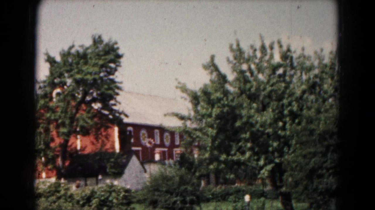Large reddish-brown building behind leafy trees and bushes.