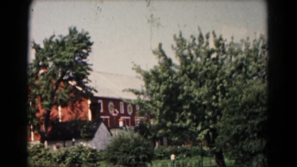 1961 Hagerstown exterior with a reddish-brown multi-story building, trees, shrubs, and a small pale structure in front.
