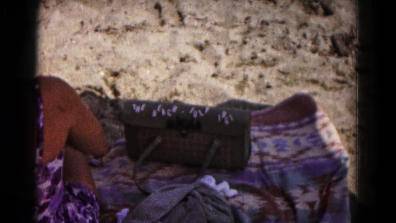 1961 beach frame showing a seated person in a purple swimsuit beside a patterned blanket and a bag marked with beach and July 1961 text.
