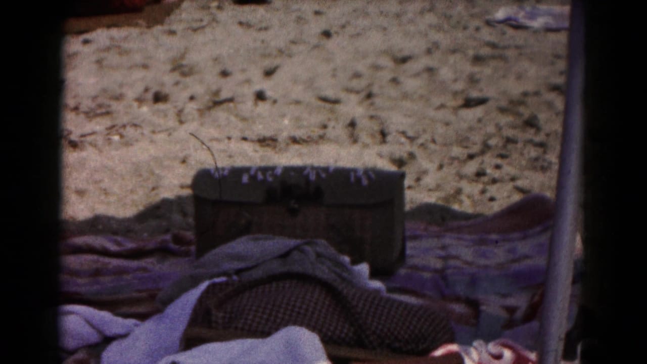 Dark storage chest and towels on sand under beach shade.