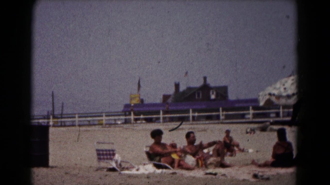 Group of adults sits and reclines on beach towels with a striped chair nearby.