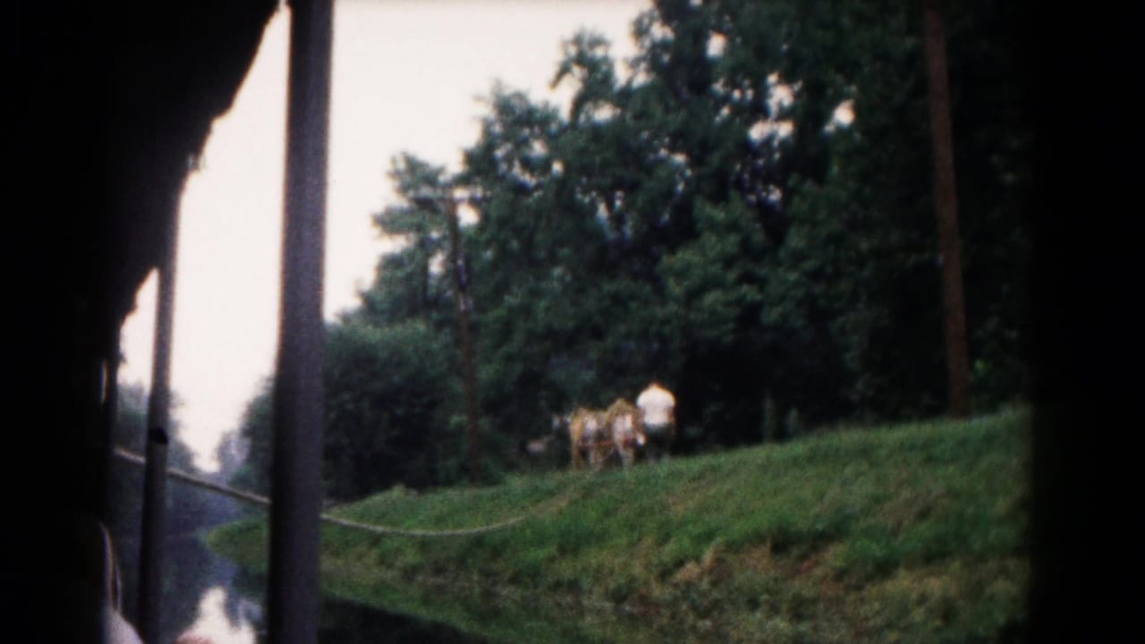 Passenger-view 8mm still from a 1961 Hagerstown train ride, looking past a post toward horses and a man on a green hillside.