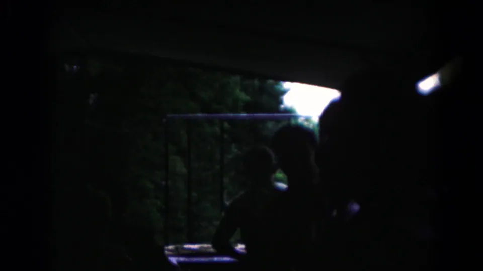 Final 1961 home-movie frame shifts into a dark ferry or vehicle interior with railings and a silhouetted seated person.