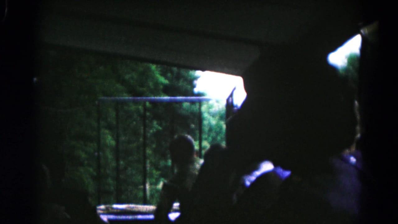 In 1961 Maryland 8mm footage, boys are silhouetted inside a dark vehicle or structure while looking toward trees beyond a railing.