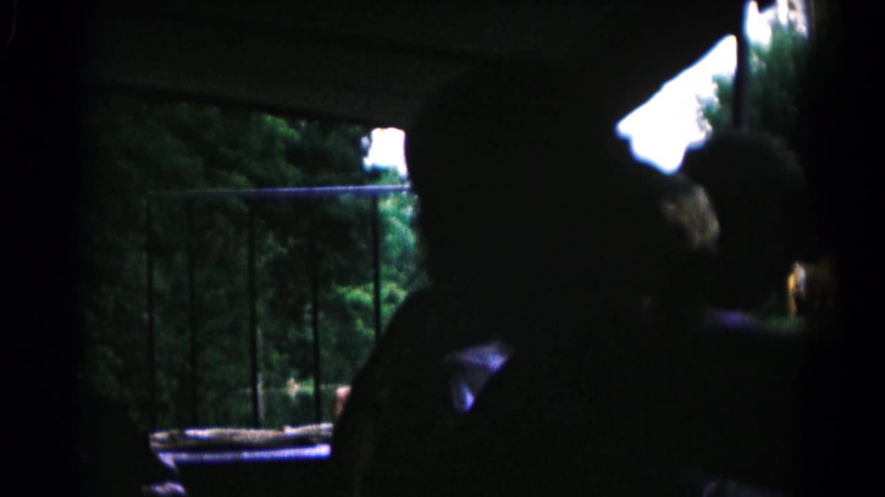 Multiple boys appear as dark silhouettes inside a shaded space, looking toward a railing and trees in 1961 Maryland home-movie footage.
