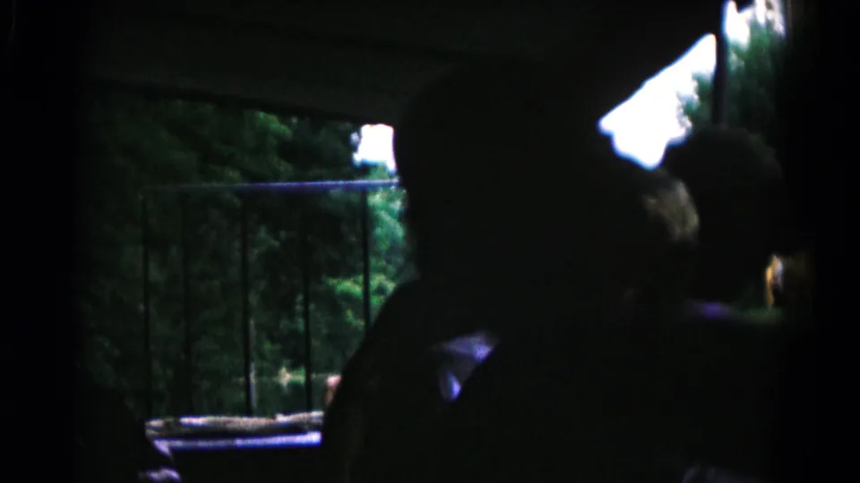 Multiple boys appear as dark silhouettes inside a shaded space, looking toward a railing and trees in 1961 Maryland home-movie footage.