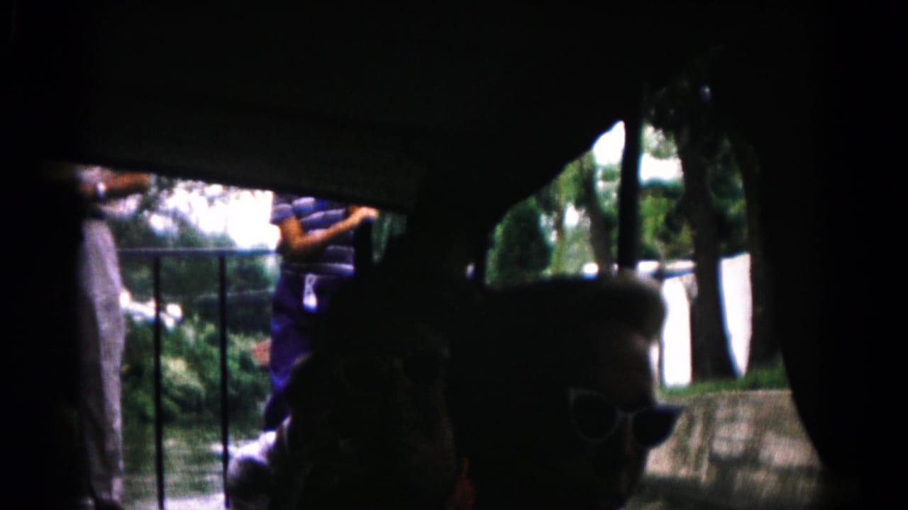 Inside the 1961 8mm boat scene, a passenger wearing sunglasses is silhouetted against a platform and trees outside.