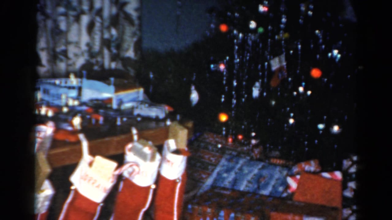 Christmas tree with tinsel, wrapped presents, and red stockings in a dim interior.
