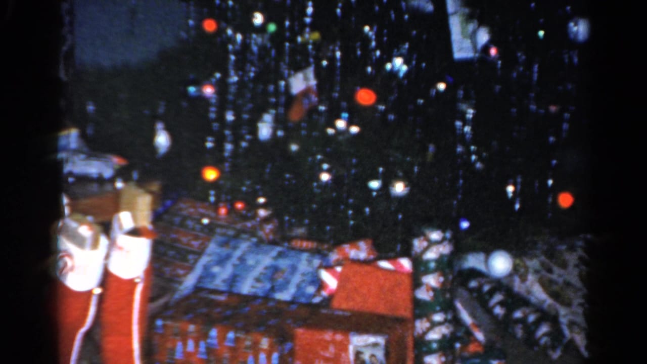 1962 Catskill holiday interior with a dark tinsel tree, wrapped presents, and stockings visible at the base.