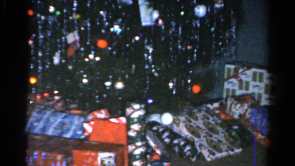 1962 Catskill home-movie view of a Christmas tree with gifts spread across a patterned floor covering.