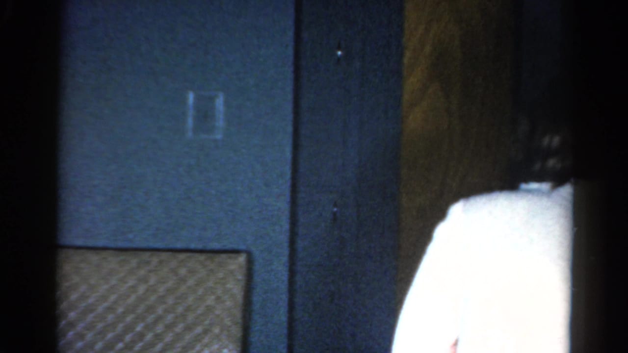 Blue interior wall and doorway as a woman in a white sweater begins to pass out of frame.