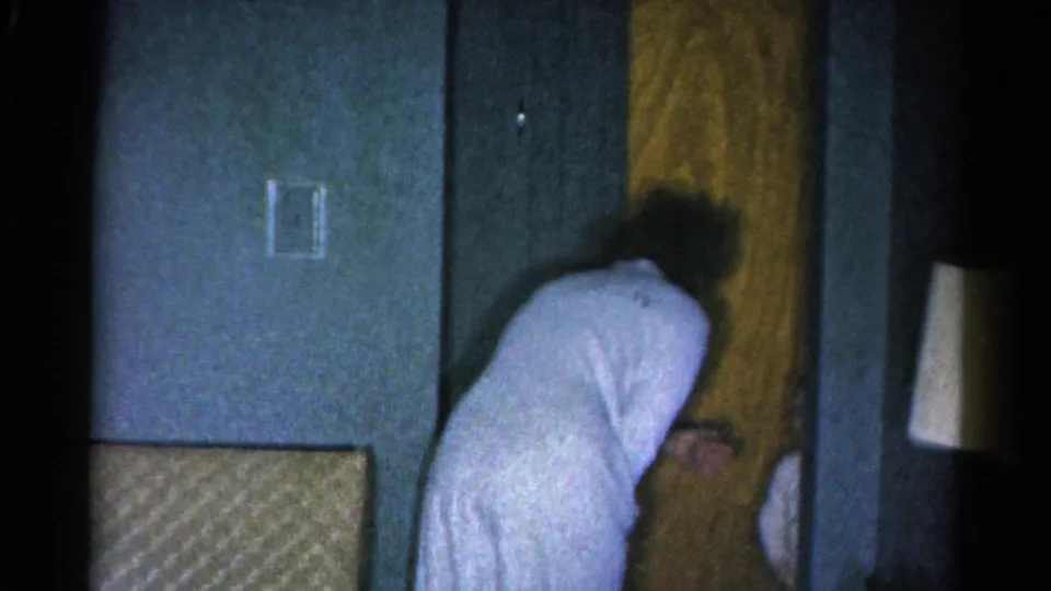 1962 Catskill frame showing the woman leaning near the wooden door, with a blue wall and shadowed interior framing the action.