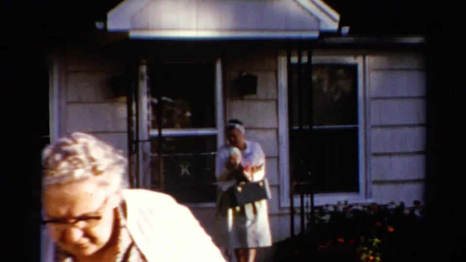 The older woman passes out of view while the younger woman remains near the front walk, holding a purse outside the house.