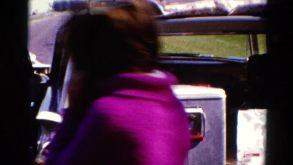 A person in a bright pink top moves near the car and cooler during the 1962 Catskill roadside home-movie scene.