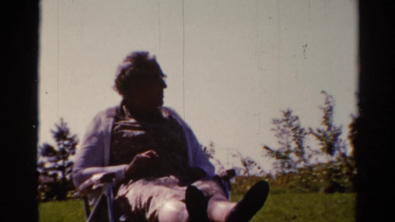 The adult man remains seated outdoors in the Catskill setting, with legs extended and trees behind him in soft 8mm color.