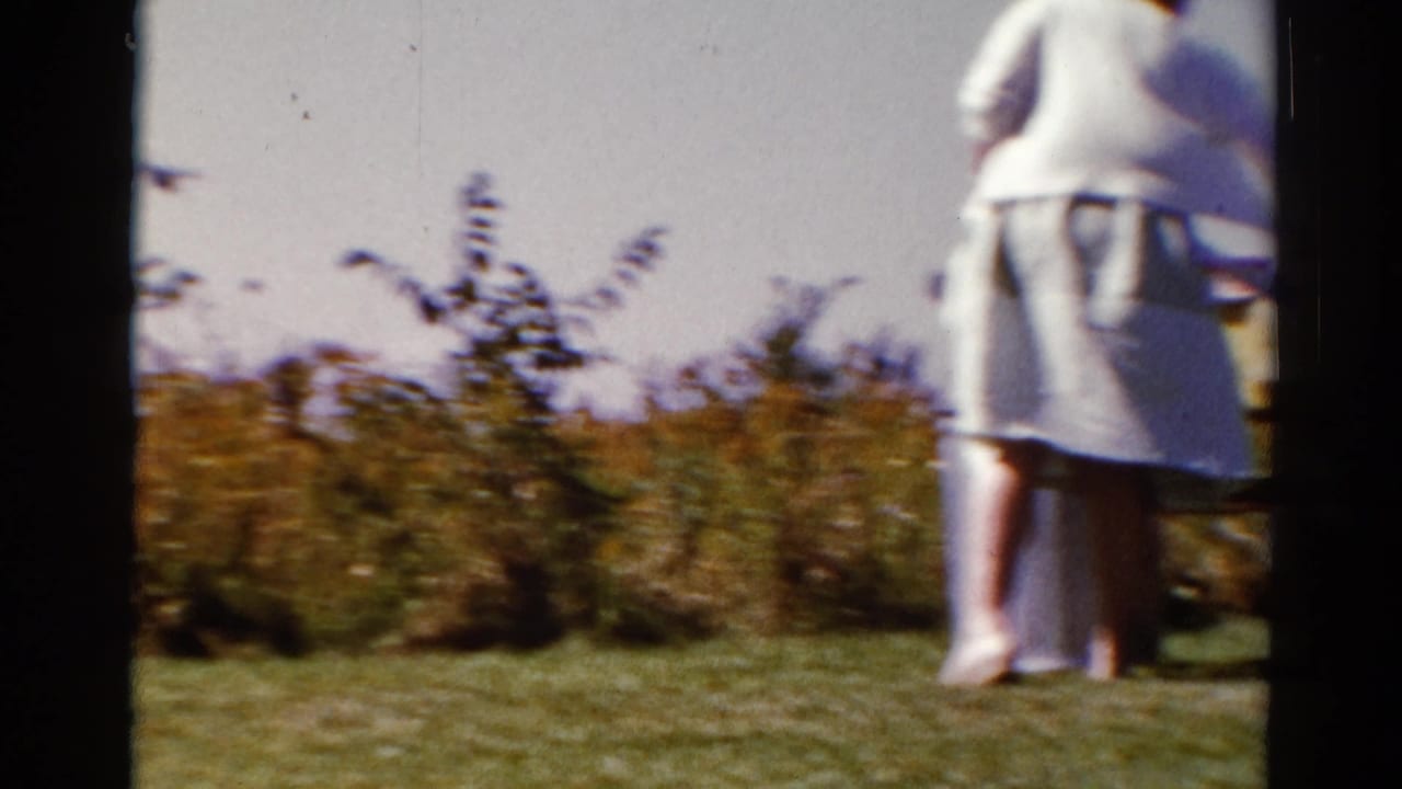 Woman in light clothing stands near a picnic table in a grassy clearing.