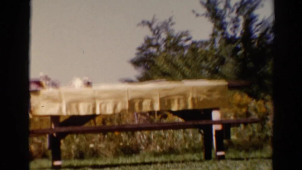 1962 Catskill picnic table cutaway with a yellow cloth, dark railing, green grass, and trees in the background.
