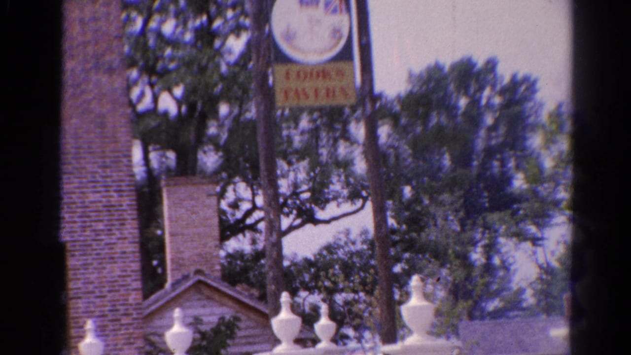 Brick building with black shutters, white fence, trees, and a hanging Cooks Tavern sign.