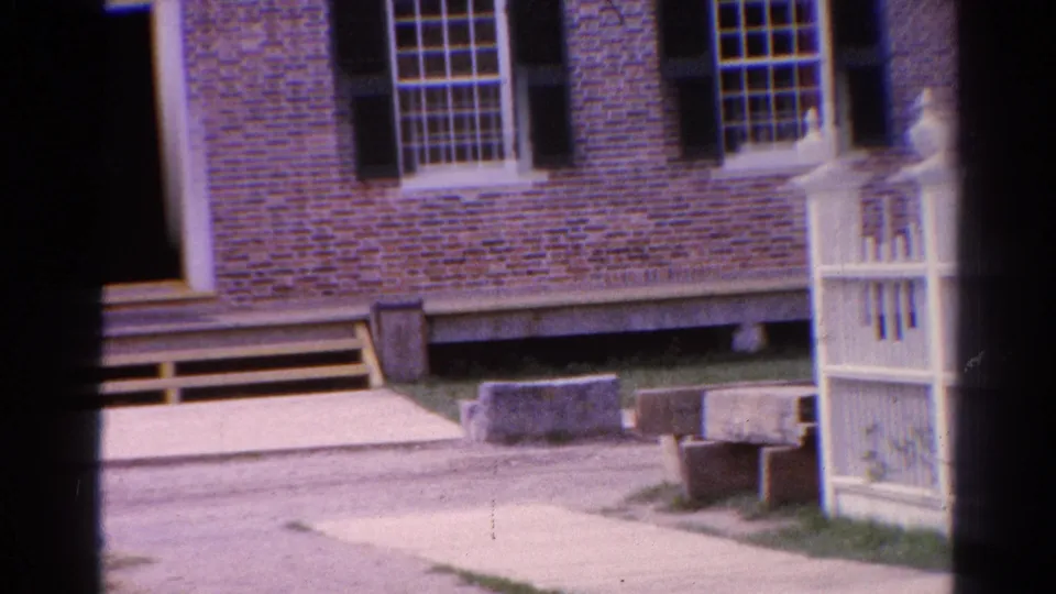 Catskill, New York 8mm frame showing a brick exterior, white fence gate, wooden steps, stone blocks, and shuttered windows.