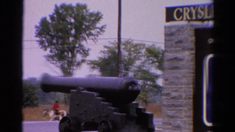 1962 Catskill, New York frame showing the cannon beside a partially readable stone sign, with distant people on horses near the road.